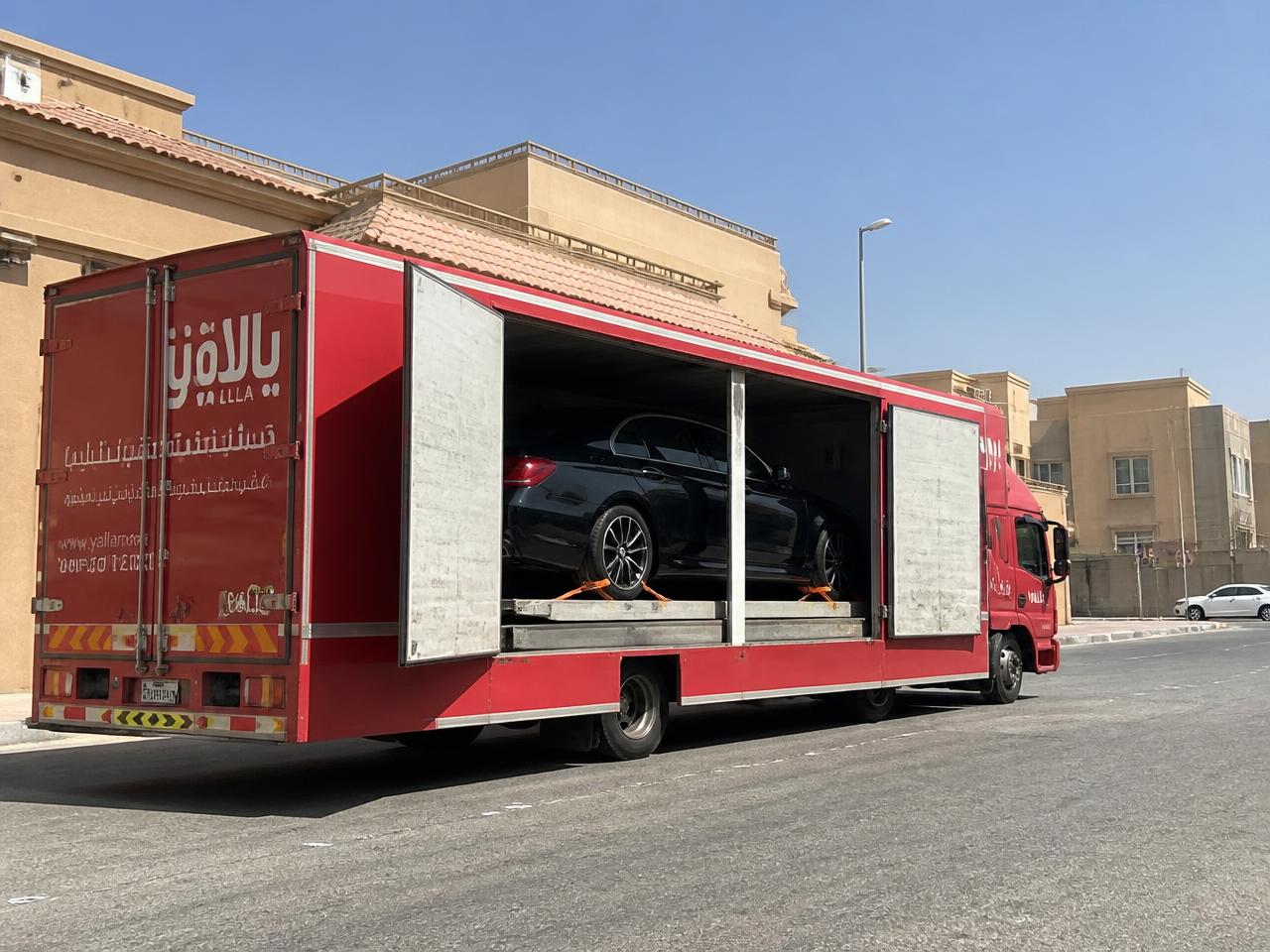 سطحة مغلقة بأبواب جانبية مفتوحة تنقل سيارة فاخرة داخل حي سكني